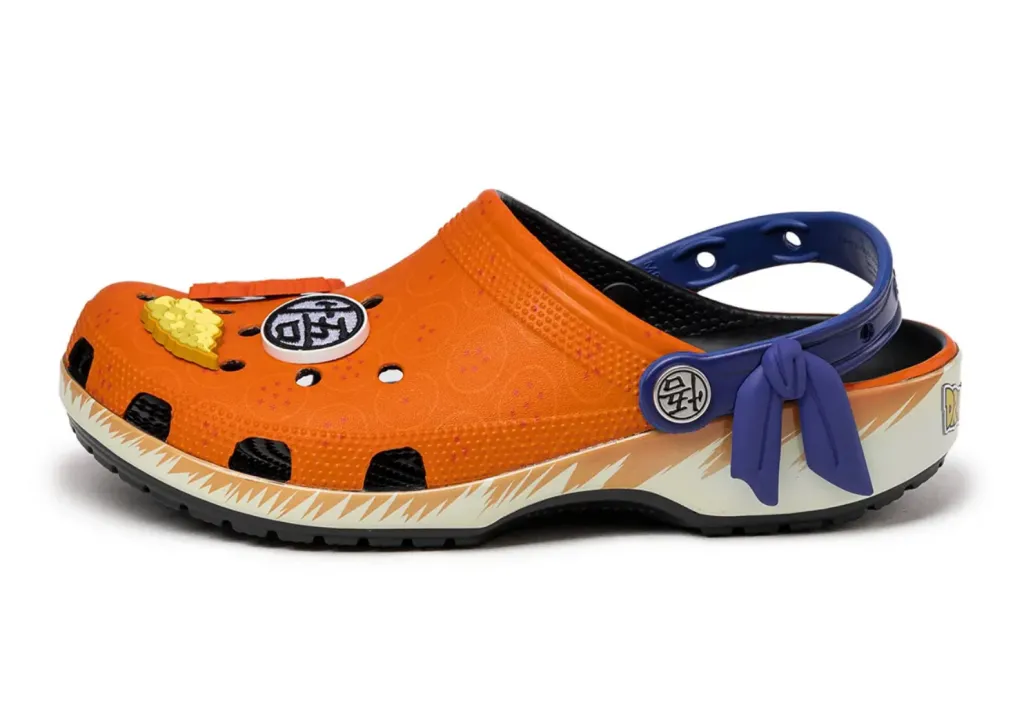 A side view of the "Blerd Kicks: Dragon Ball Z x Crocs Classic Clog," highlighting the vibrant orange base and electric blue accents that mimic Goku's iconic gi. The perforated upper includes fun Jibbitz charms, such as the Four-Star Dragon Ball and Capsule Corp logo, adding a playful nod to the Dragon Ball Z series. The curved sole and ergonomic design ensure both style and all-day comfort for fans on the move.